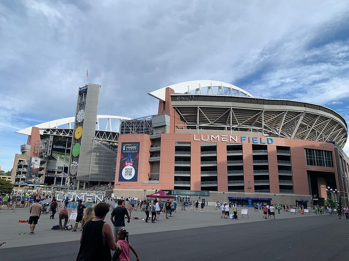 A crowd of people arrive at a large stadium for a sporting event.