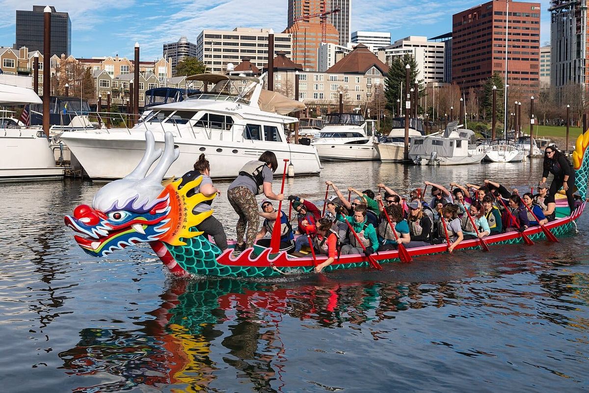 A large group of people paddle a large, colorful dragon boat with an elaborate head on its bow.