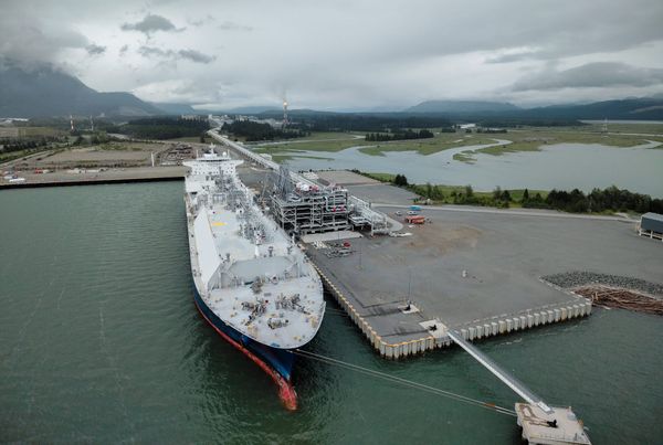 A massive LNG tanter ship docked in a port with rain clouds and low mountains in the distance.
