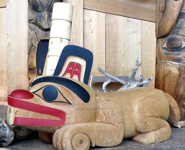 An Haida-style sculpture of a beaver in wood, with stylized eyes, mouth, teeth, and ceremonial hat.