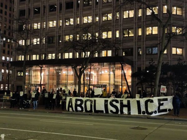 Protesters in front of a brightly lit building at night hold sign that reads Abolish ICE