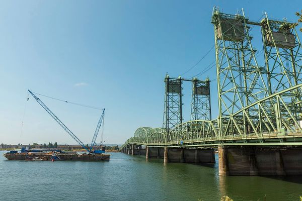 A long, cantelievered freeway bridge over a river, with a barge next to it.