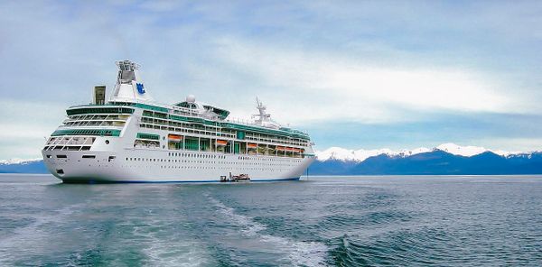 A massive cruise ship leaves behind wake in an inland sea with a snowy mountain range in the distance