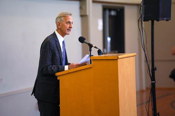 A man in a suit stands behind a podium giving a speech