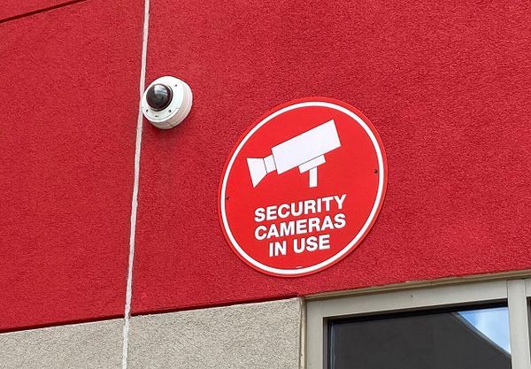 A dome-style secruity camera above a store door with the sign that reads: security cameras in use