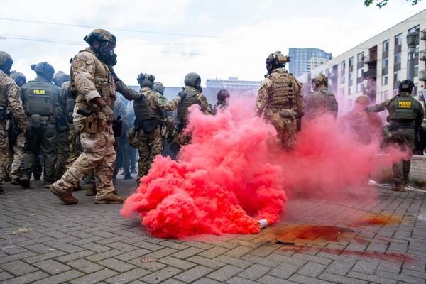 ICE goons in tactical gear deploy a canister of red-tinted gas.