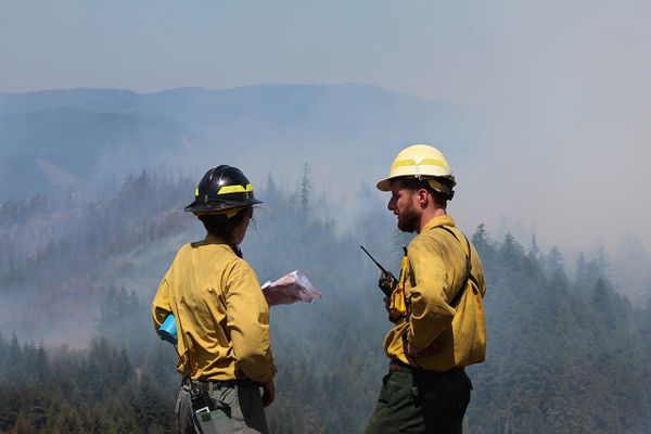 Two wildfire firefighters in front of a smoky, forested mountain
