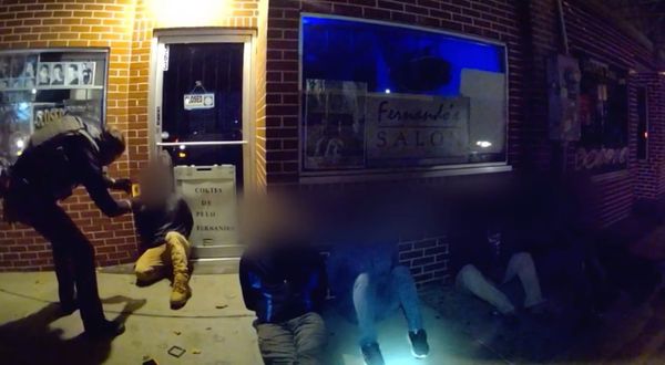 A masked goon takes a phone photo using what appears to be facial recognition technology on immigrants.