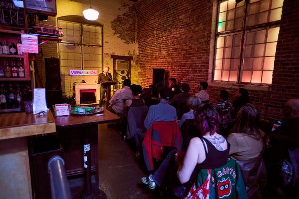 A guy stands behind a podium in a brick-walled bar in front of a full crowd of Cascadia supporters.