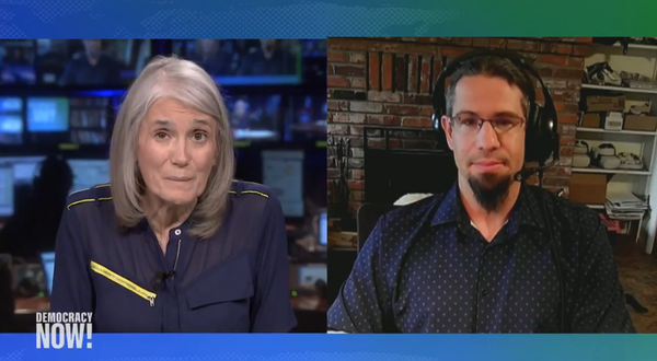 Reporter Amy Goodman speaks with a man in a button down shirt and beard via video conference.