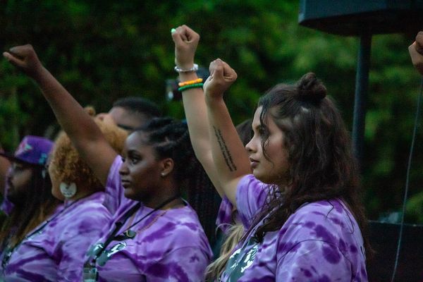 Two people in purple shirts hold their fists high as a sign of Black power and pride.