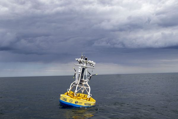 A scientific buoy with an array of monitors on top of it is seen in a wide ocean under a stormy sky.