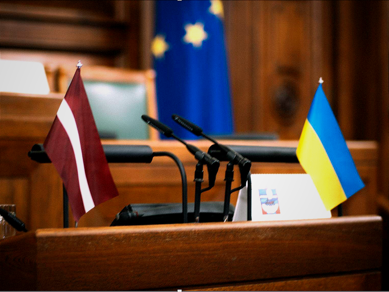 Flags of Latvia and Ukraine sit beside microphones in parliament.