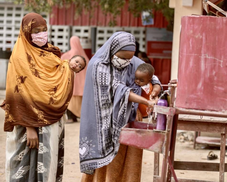 Mothers carrying babies wash their hands on arrival at a maternal and child health center in Mogadishu, Somalia