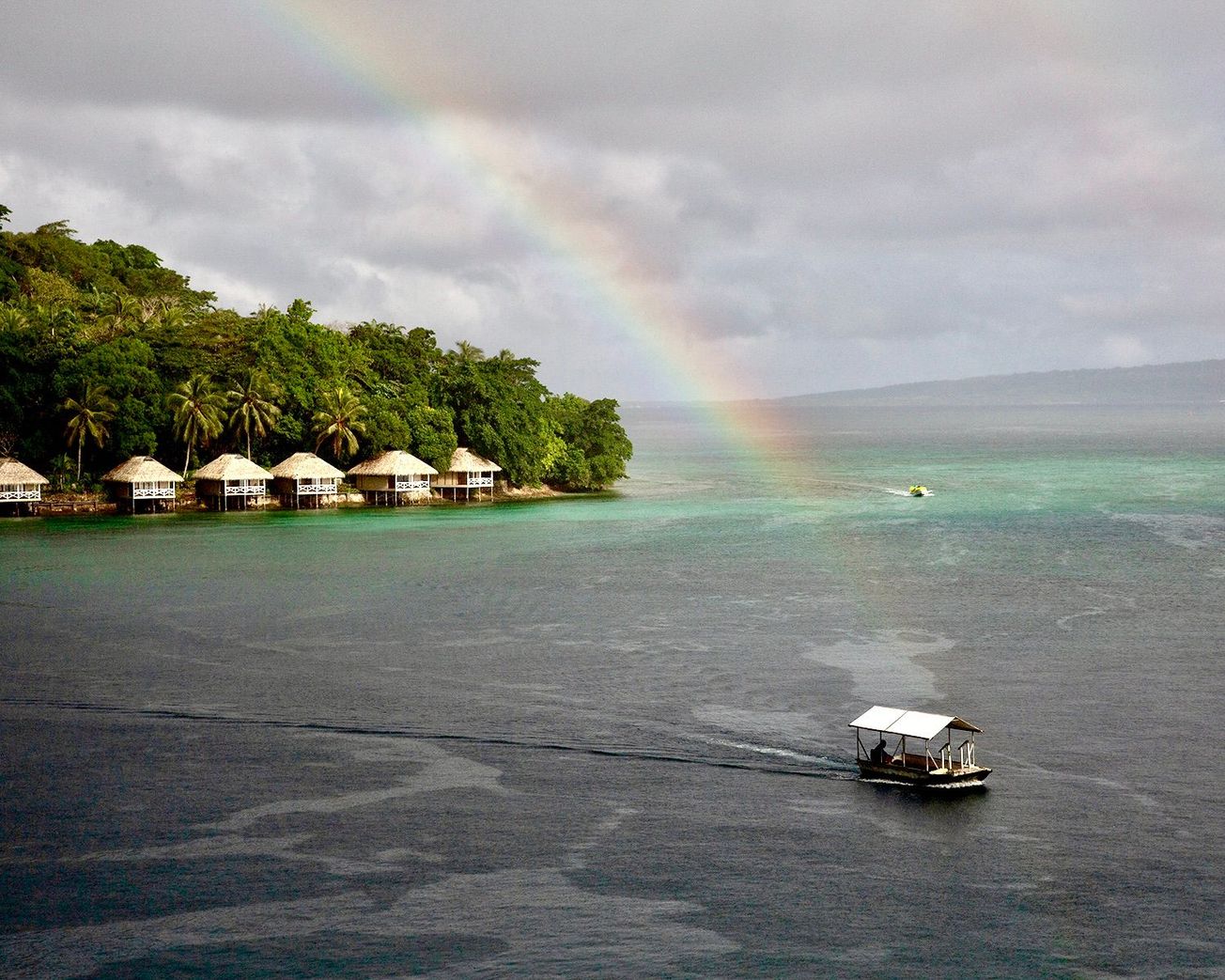 A taxi boat crosses a rainbow-lit harbor at Vanuatu