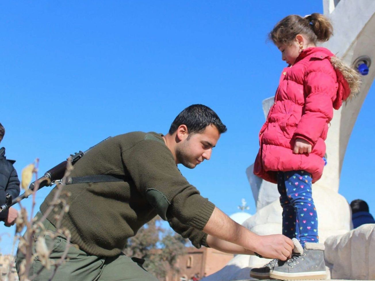 A Kurdish soldier ties a girl's shoes in northeastern Syria.