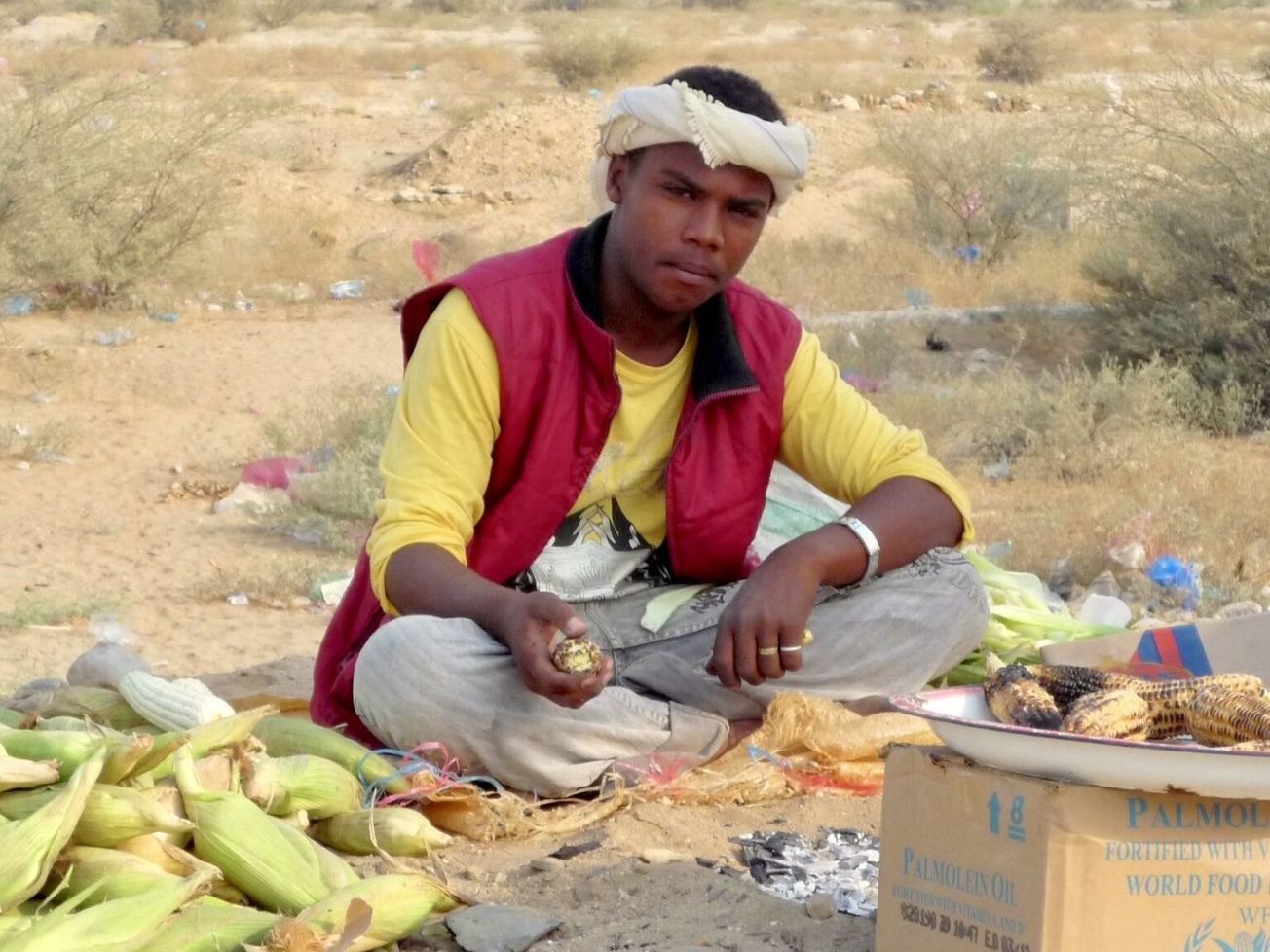 A young man prepares roasted maize atop a World Food Program carton in Yemen
