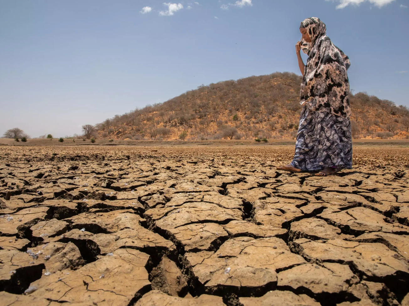 Kheira Osman Yusuf, a farmer in northern Kenya, walks across a dried-up reservoir next to her land