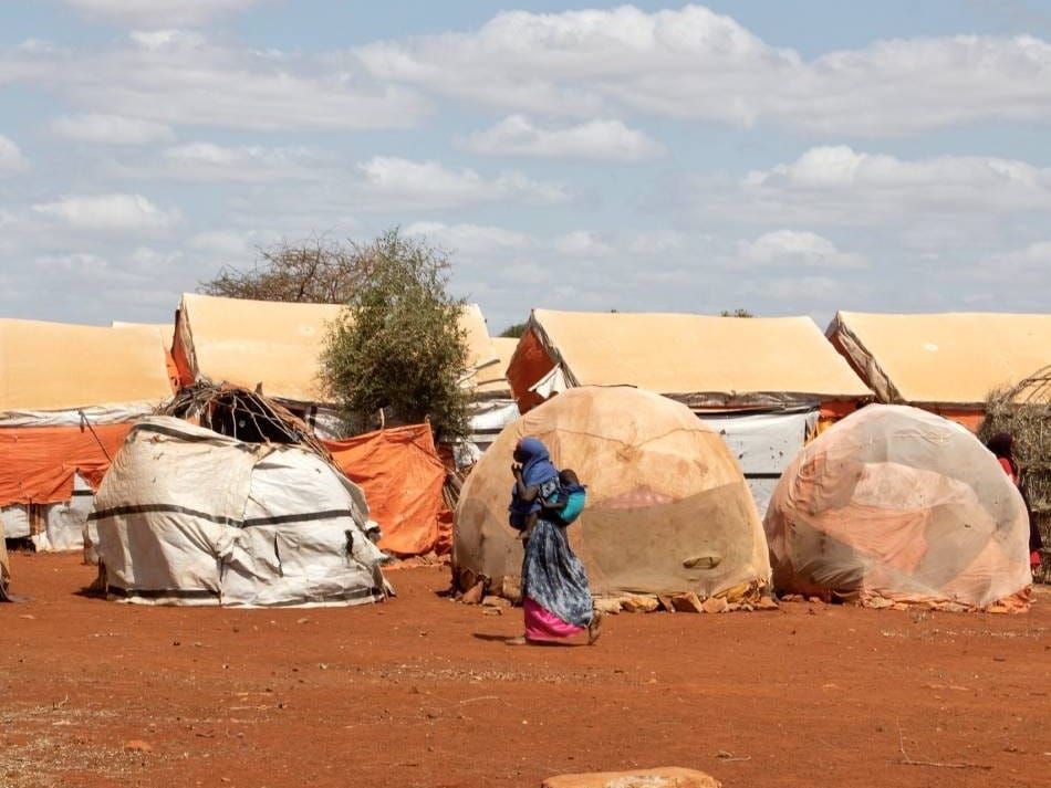 A mother carries her child past shelters in one of the hard-to-reach areas of Somalia