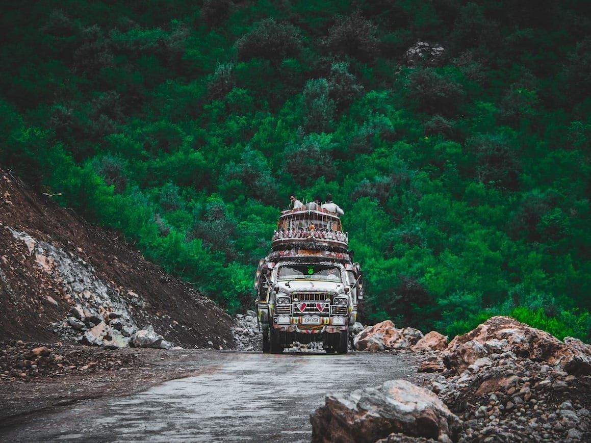 A colorful Pakistani truck grinds up a road through a forested hill