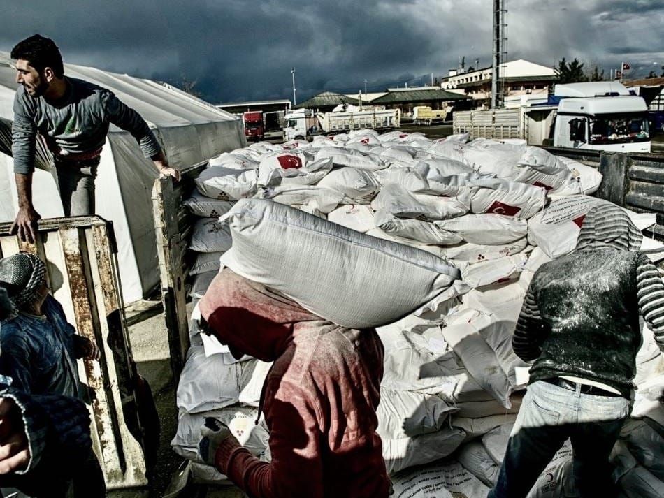 Turkish workers load bags of flour from the Turkish Red Crescent onto a truck bound for Syria
