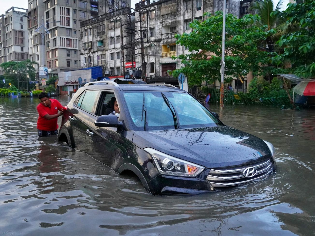 A man pushes a car with a woman in the passenger's seat along a flooded street in India.