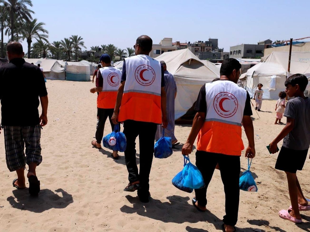 Red Crescent volunteers distribute food to displaced Palestinians in shelter camps.