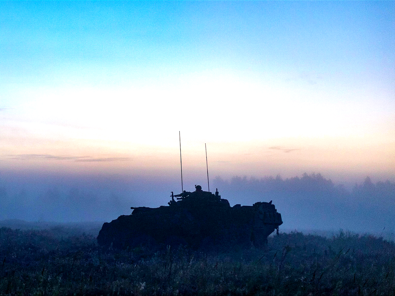 An armored vehicle patrols at sunset during an Aug. 2024 military exercise at Ādaži Military Base, home of NATO's multinational battle group in Latvia. 