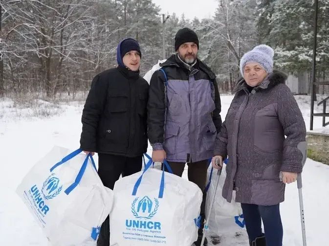 Three villagers in Ukraine's Kyiv Oblast receive winter kits from UNHCR and local partner Right to Protection in 2023 so they can insulate their damaged home.