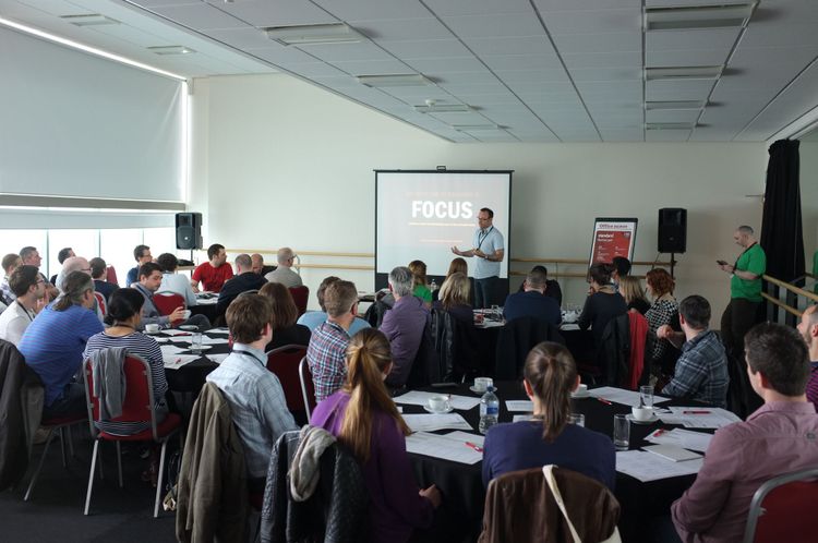 Packed conference room, people at round tables, we're behind everyone else; presenter at a screen that says FOCUS