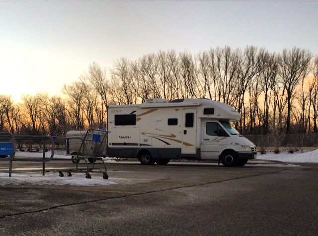 Shopping carts, grey asphalt foreground; background is white RV "swish" graphics, trees and setting (or rising) sun.