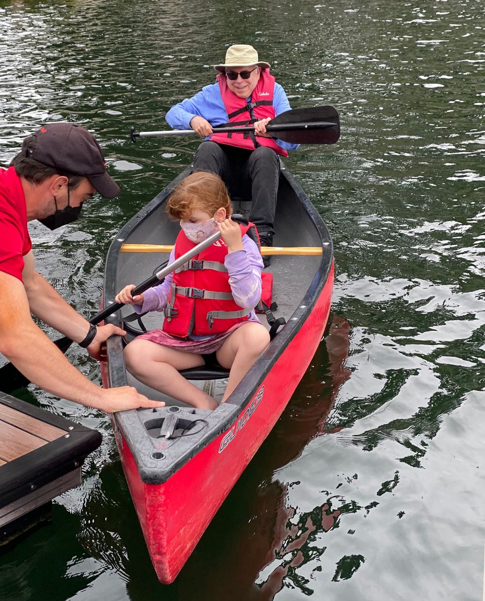 An man helping a tween girl docking a red canoe, with an older man riding in the stern