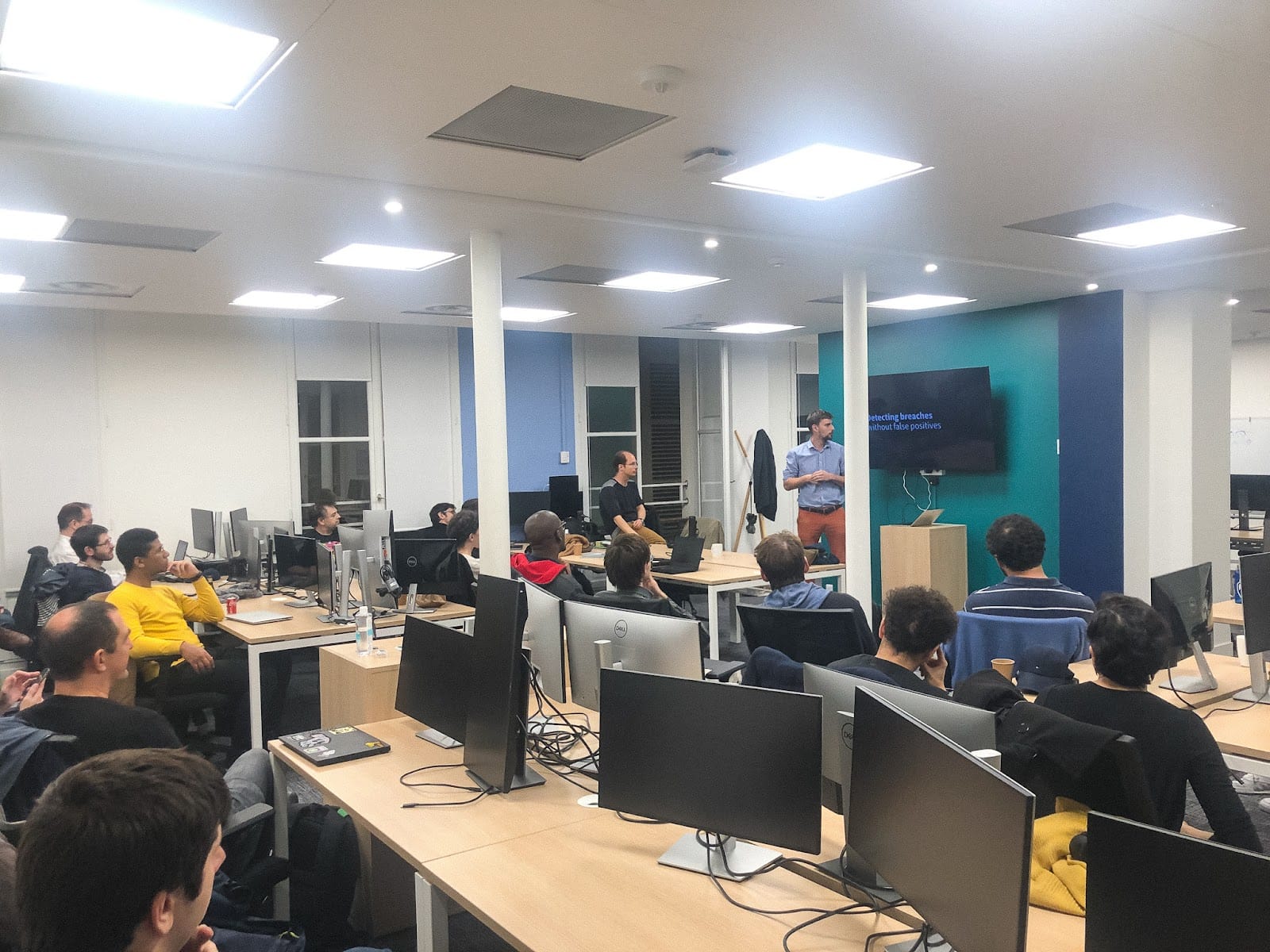 people standing around an office while a presenter stands in front of the room
