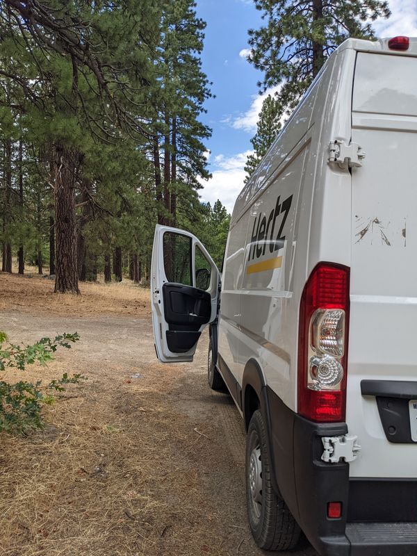 The rental van with door open parked in a forest 