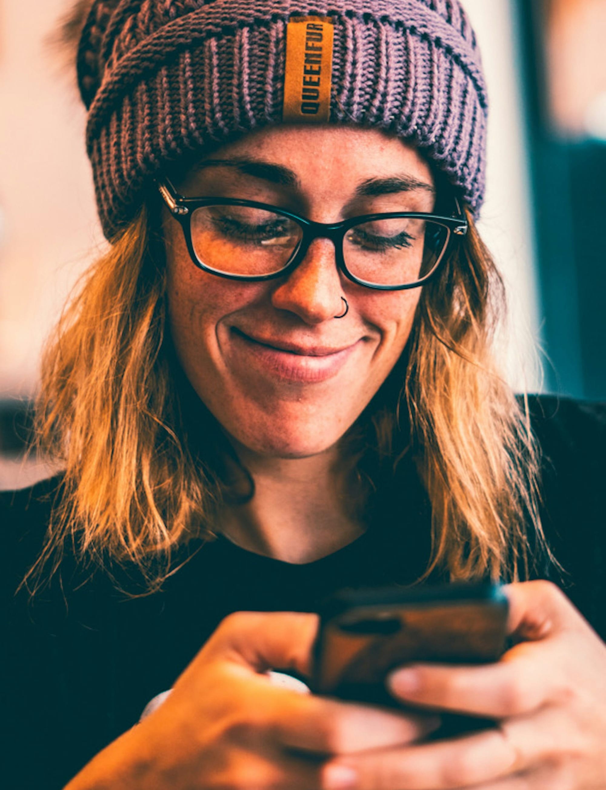 woman wearing black framed eyeglasses and grey knit beanie while using smartphone