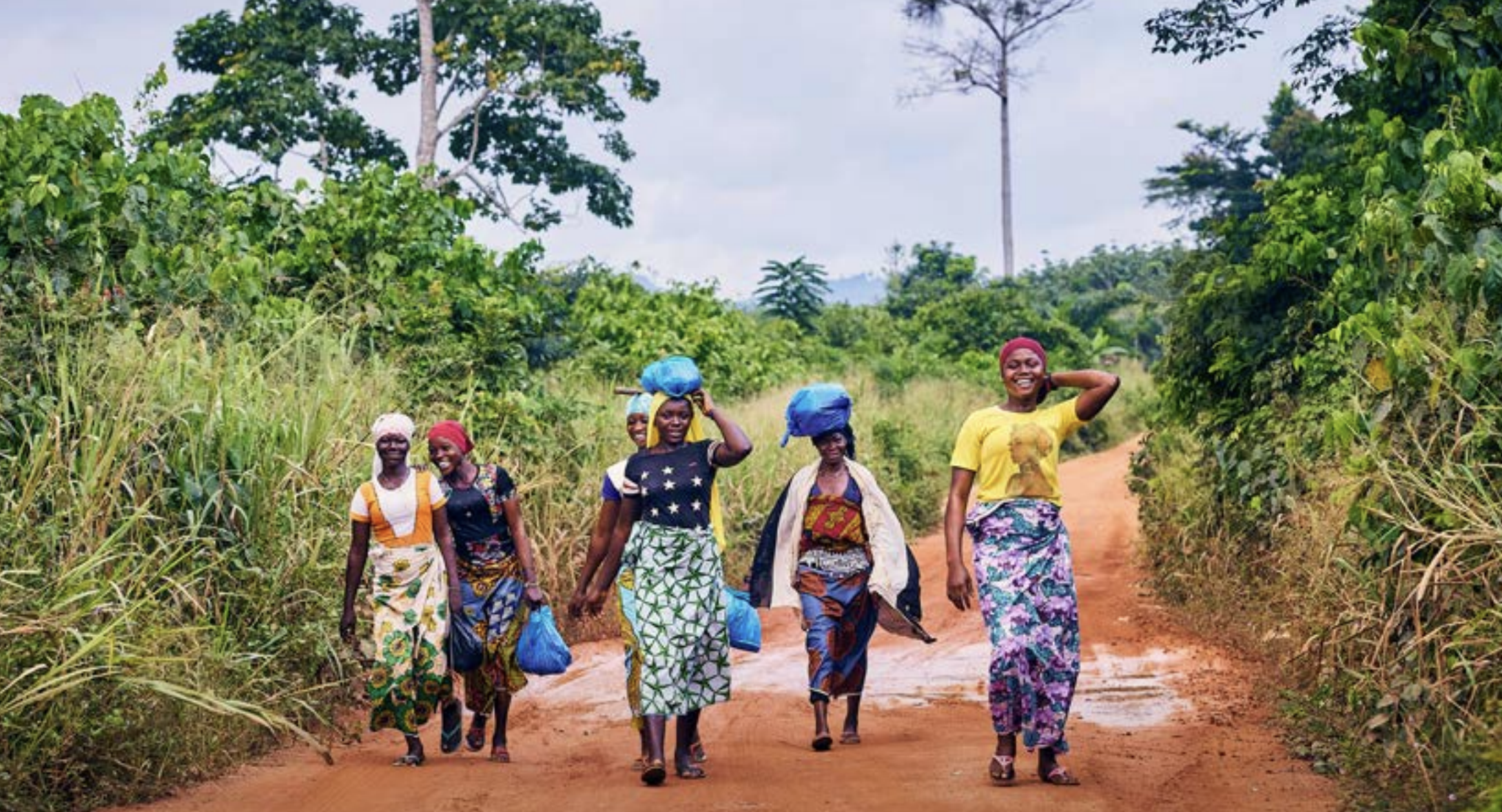 Image shows a group of female cocoa farmers walkig along a road.