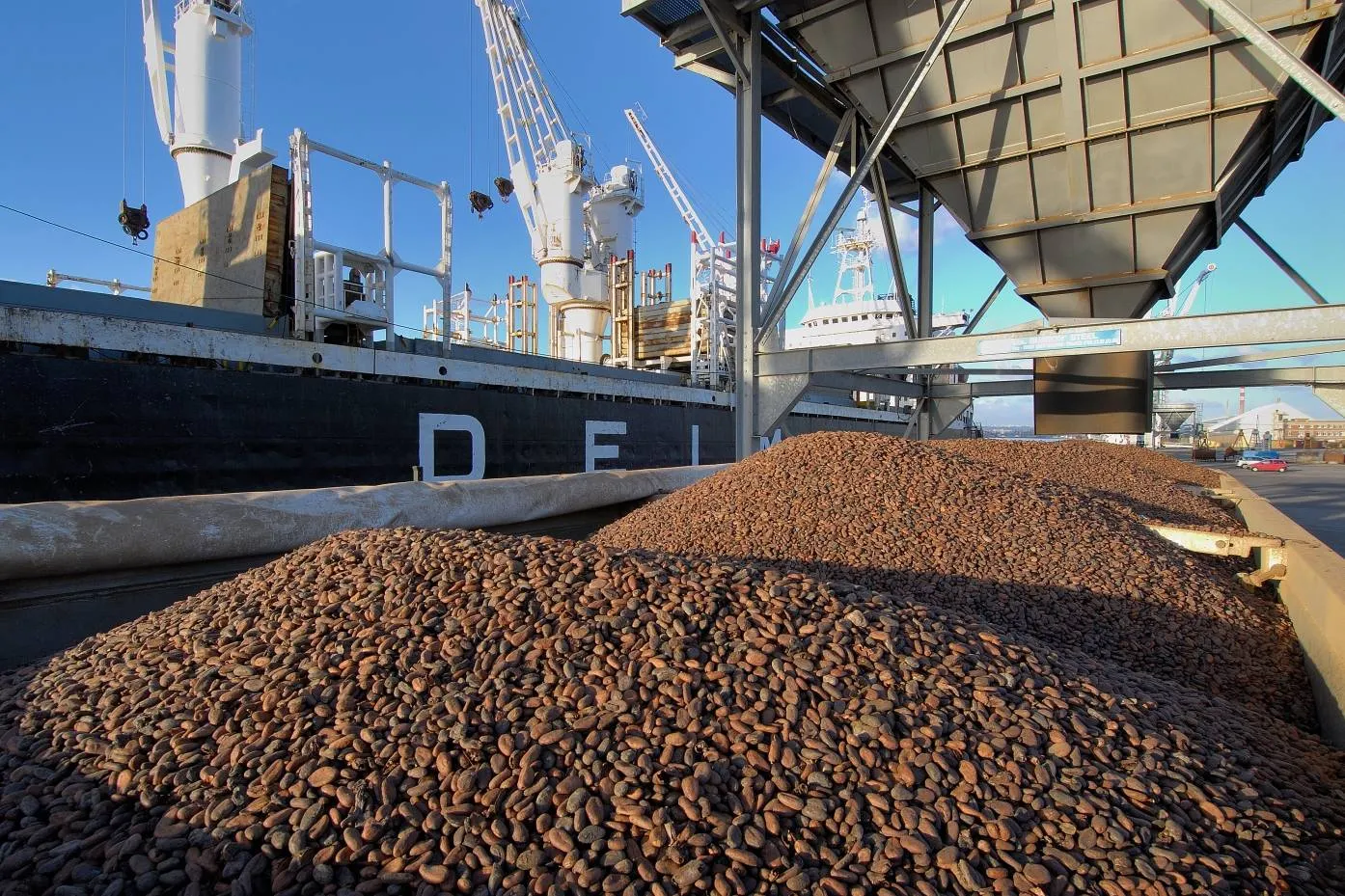 Image shows cocoa beans at a port being loaded onto a boat.