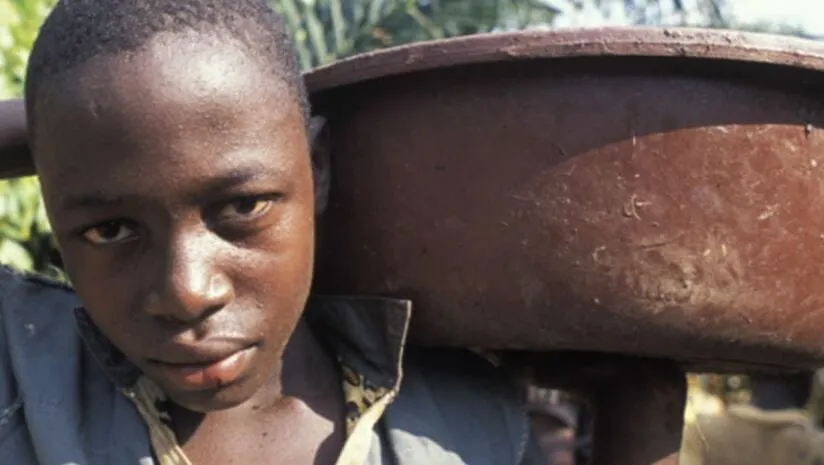 Image shows a young boy carrying a heavy bucket on a farm in Africa.