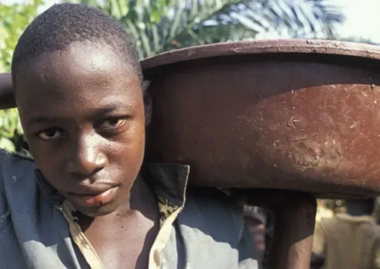 Image shows a child in West Africa carrying a heavy tray on his shoulders.