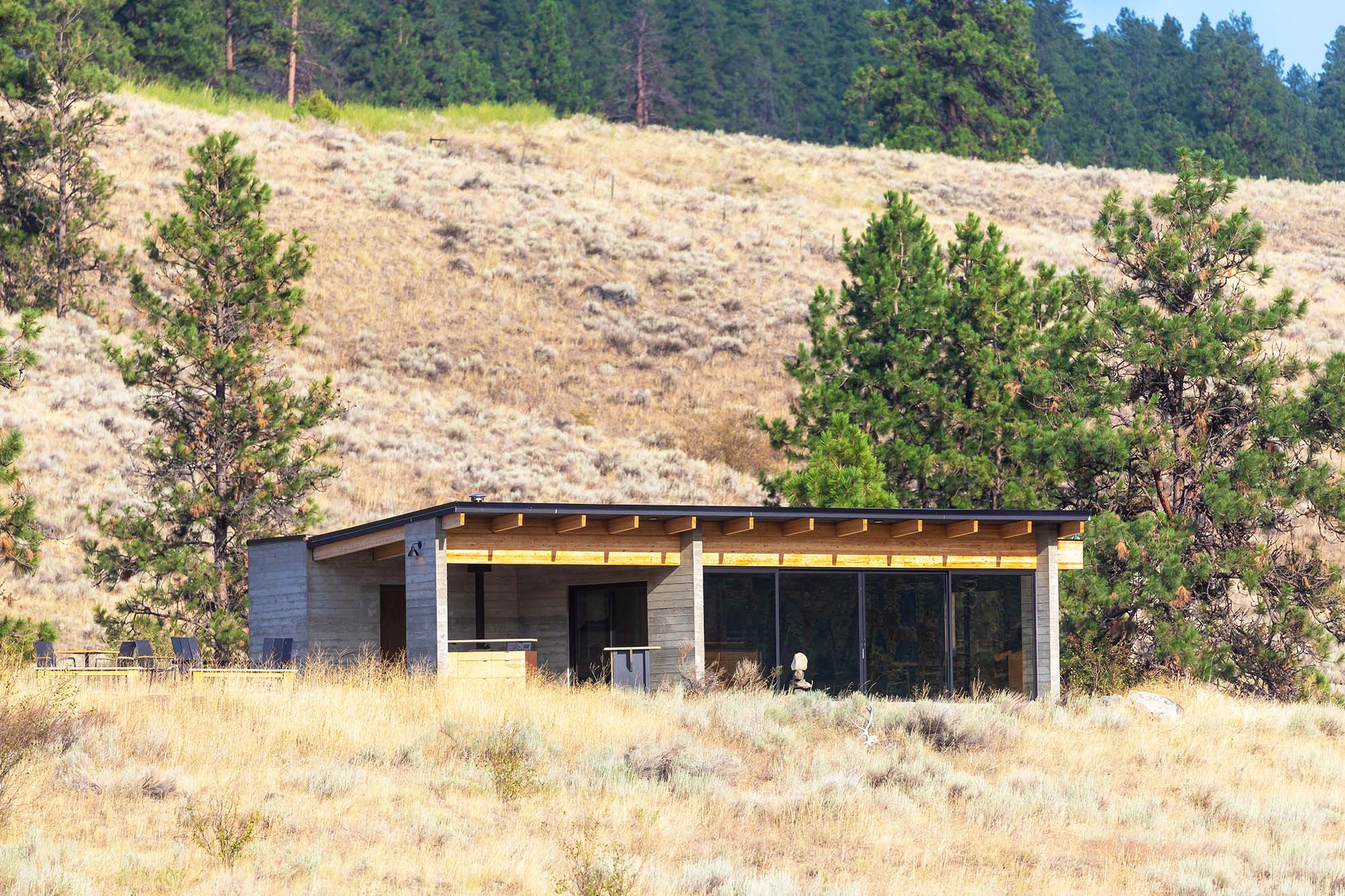 A building set among dry golden grassland and every green trees, below a hillside