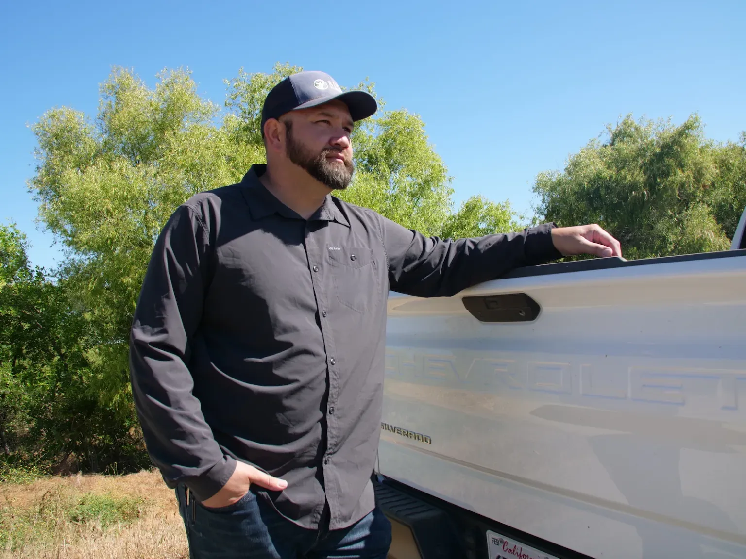 A person in ball cap standing outdoors, leaning against a white pickup truck