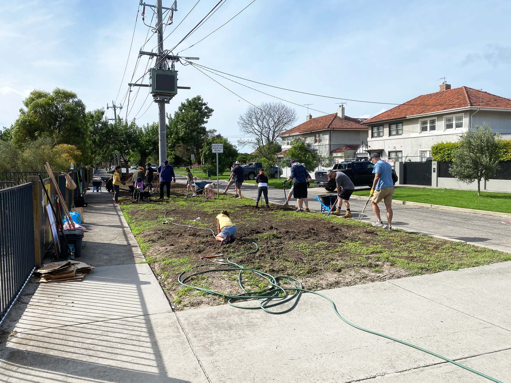 A gropu of people gardening in a grassy verge between a road and sidewalk
