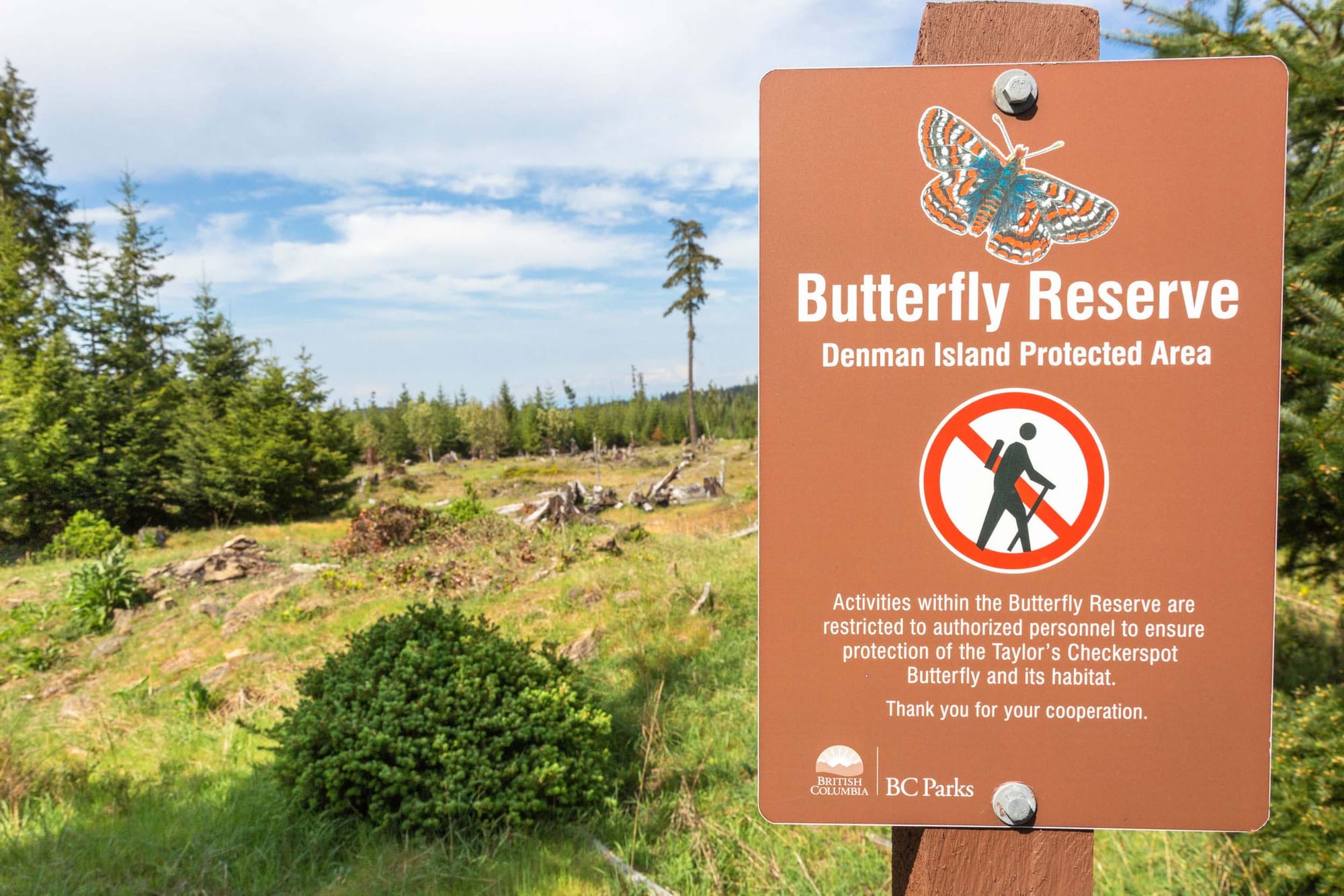 A sign outdoors reads "Butterfly Reserve: Denman Island Protected Area"
