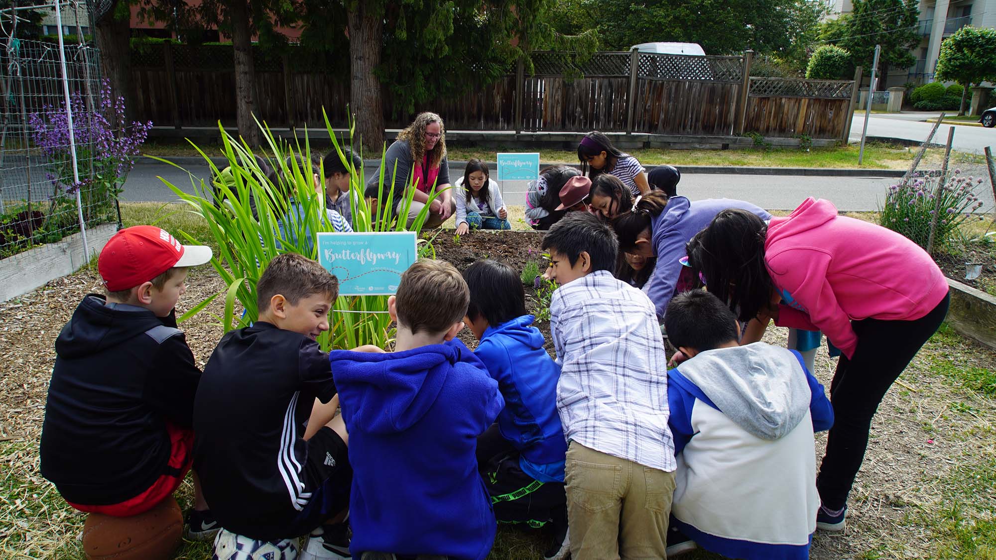 A group of children and adults surrounding raised garden beds in an urban environment