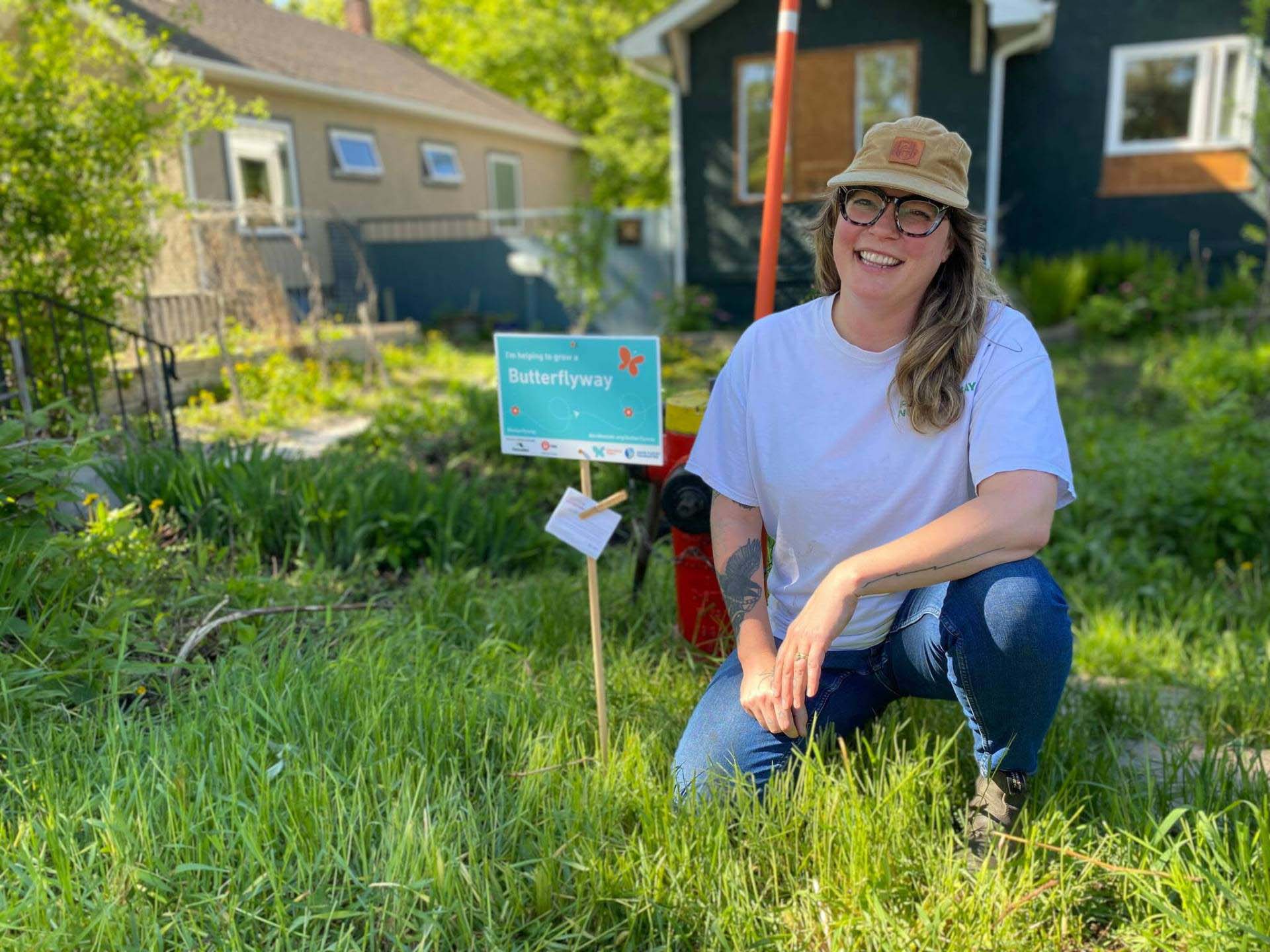A person wearing glasses crouched in a front yard with a butterflyway sign