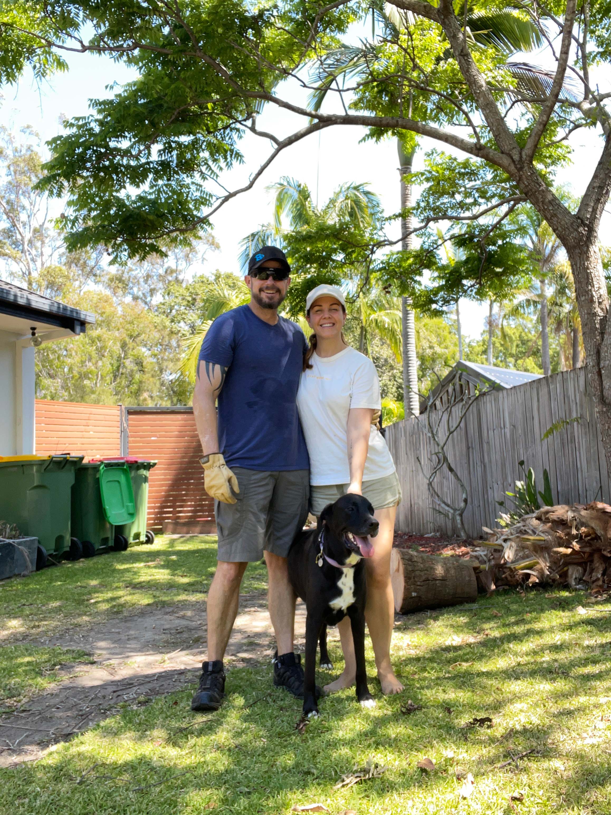 Two people and a dog posing in a yard and smiling