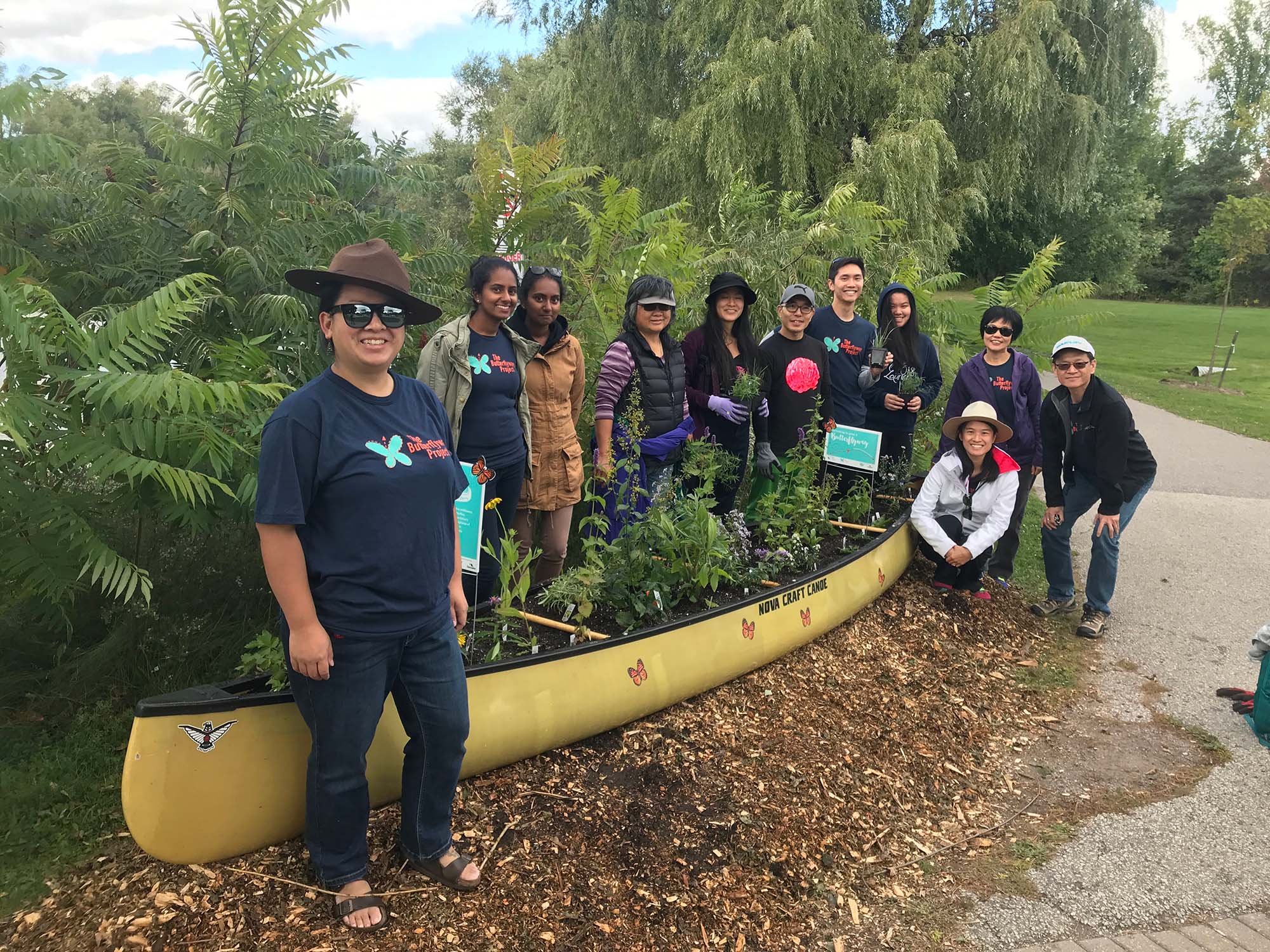 A group of people posing in a park next to a yellow canoe planted with native plants