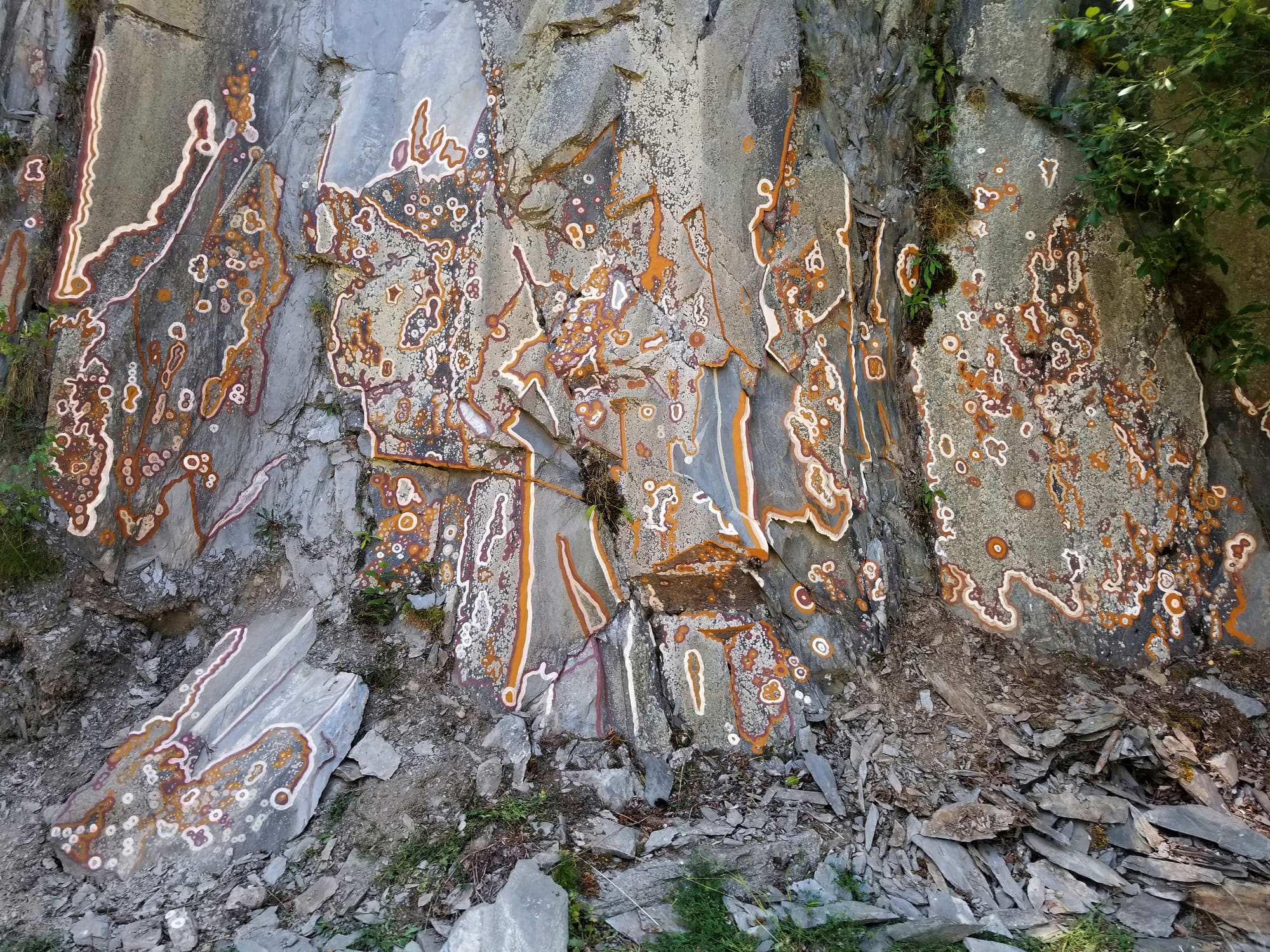 A grey cliff face painted with abstract designs in white and earth colours