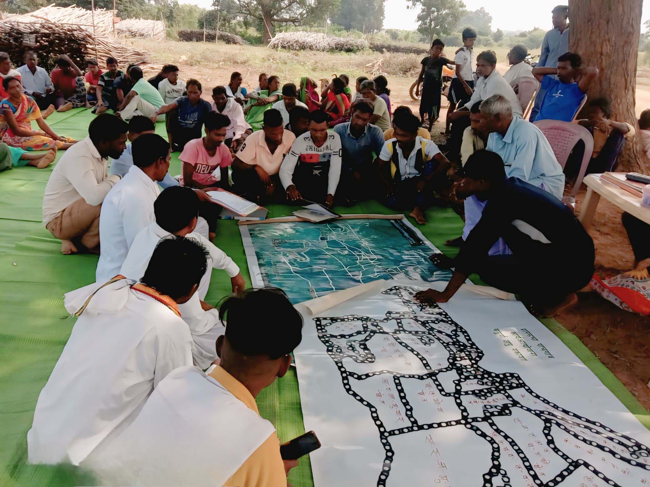 A group of people outdoors, sitting on covered ground looking at large maps