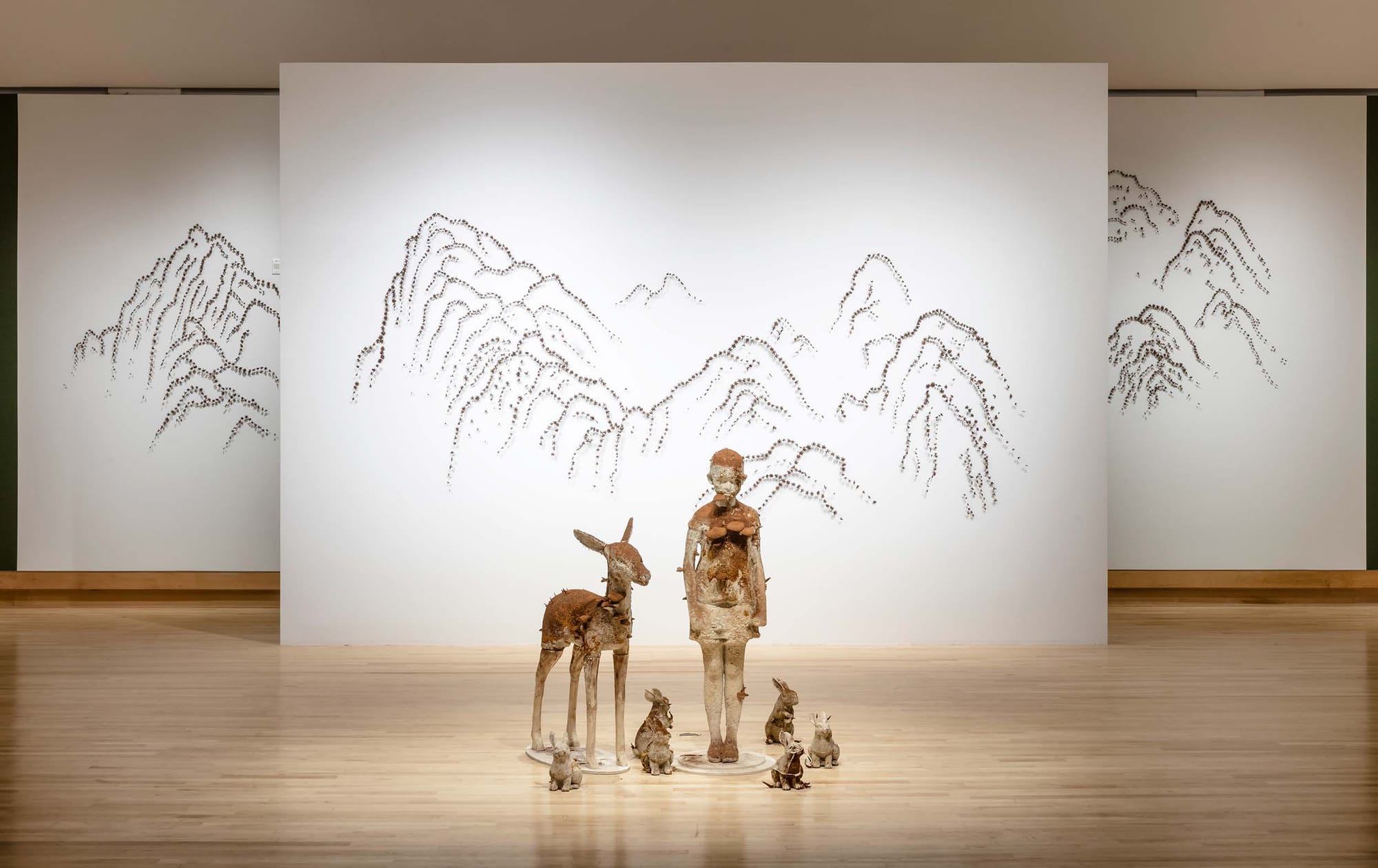 An art gallery with hardwood floors. Several natural-looking sculptures stand in front of white backgrounds decorated with mountain shapes.